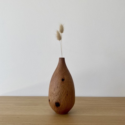 Vaso de madeira castanha com ramos secos, em cima de superfície de madeira clara