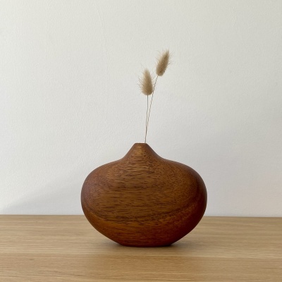 Vaso de madeira castanha arredondado com dois ramos secos numa superfície de madeira clara