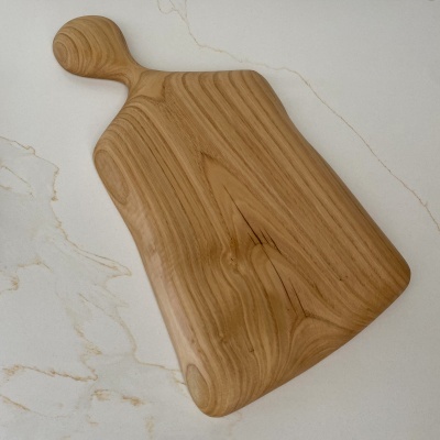 Tábua de cortar de madeira com cabo arredondado sobre uma superfície branca marmoreada