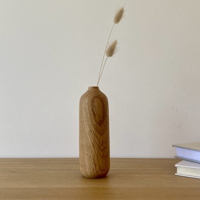 Vaso cilíndrico de madeira com duas flores secas em cima de mesa de madeira