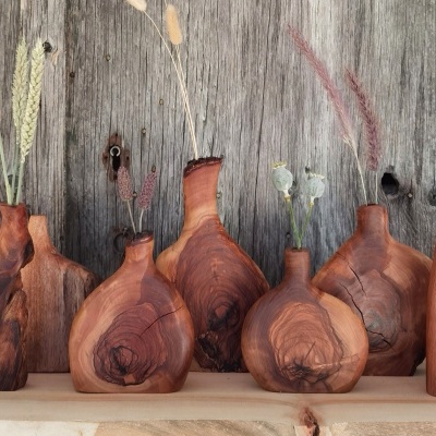 Seis frascos de madeira com ramos secos numa prateleira de madeira