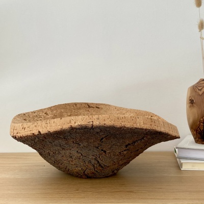 Escultura decorativa de madeira natural com textura rústica sobre mesa de madeira com livros e vaso ao fundo