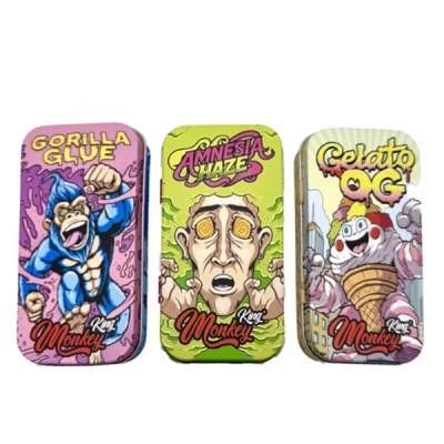 Três caixas metálicas coloridas com designs de banda desenhada e nomes GORILLA GLUE, AMNESIA HAZE e Gelato OG.