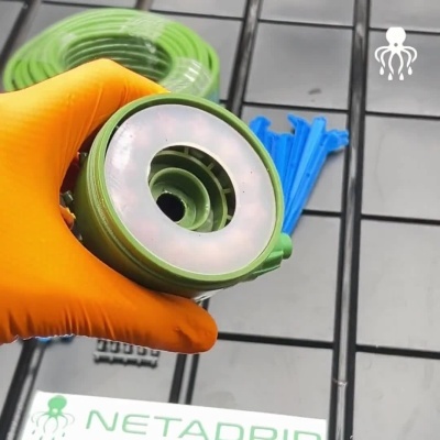Mangueira de jardim verde com conectores azul e verde segurada com luva laranja sobre azulejo cinzento
