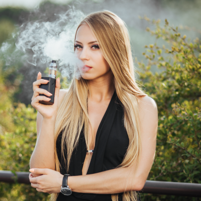 Mulher loira com top preto a usar cigarro eletrónico ao ar livre