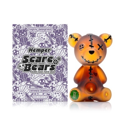 Cachimbo em forma de urso teddy translúcido laranja e castanho com remendos e embalagem roxa desenhada.