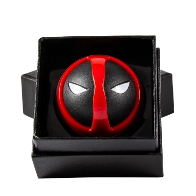 Objeto redondo preto e vermelho dentro de caixa preta, com design semelhante à máscara do Deadpool