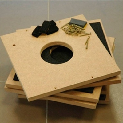 Placas de MDF quadradas empilhadas com buraco no centro, pedaços de feltro, esponja e pregos em chão de azulejo cinza.