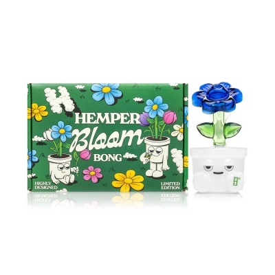 Bong de vidro com base branca e tampa azul em forma de flor ao lado de caixa verde decorada com flores e texto