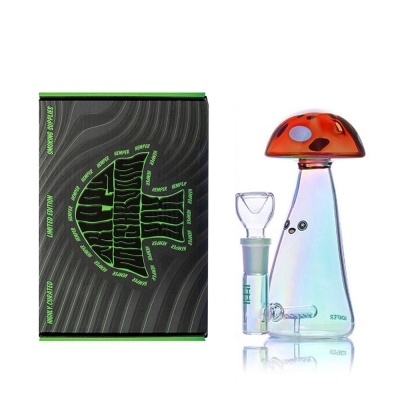 Peça de vidro para fumar em forma de cogumelo ao lado de caixa preta com texto verde.