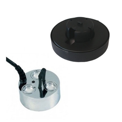 Base metálica prateada com três orifícios e cabos pretos ao lado de tampa preta redonda