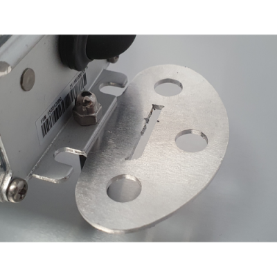 placa metálica oval prateada com três buracos circulares e entalhe central fixada a superfície branca