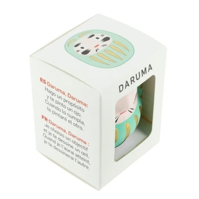 Caixa branca com figura Daruma verde água e dourada visível através de janela