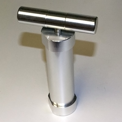 Dispositivo metálico prateado com barra horizontal e base hexagonal.