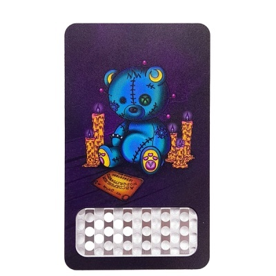 Urso azul costurado com alfinetes, velas amarelas, tábua Ouija e base roxa.