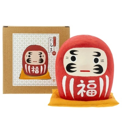 Figura Daruma vermelha com tecido amarelo em caixa de cartão