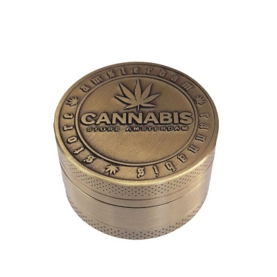 Moedor de metal dourado com texto e folhas de cannabis gravadas