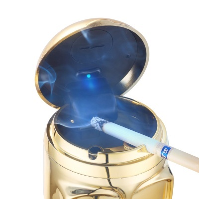 Cinzeiro dourado metálico com tampa aberta e cigarro aceso