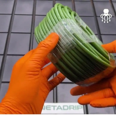 Mangueira verde enrolada segurada com luvas laranja sobre grelha preta com texto NETADRIP.