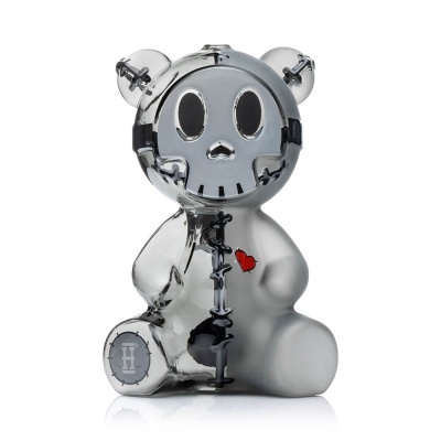 Figura decorativa de urso metálica prateada com costuras pretas e coração vermelho.