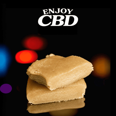 Duas barras bege claro com mordida e texto ENJOY CBD com fundo preto e luzes coloridas.