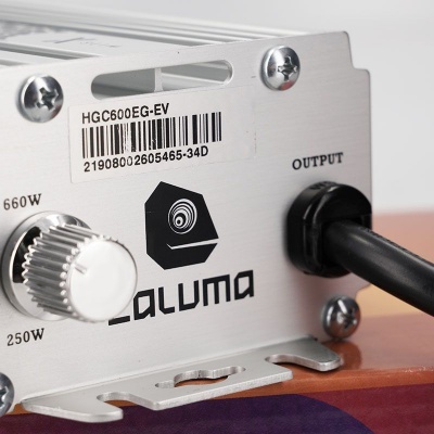 Dispositivo eléctrico metálico prateado com botão branco, etiqueta com código de barras e porta de saída com cabo preto