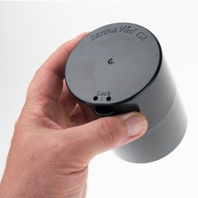 Mão segurando recipiente preto com tampa onde está escrito 'Camera Vét C2' e indicação de Lock.