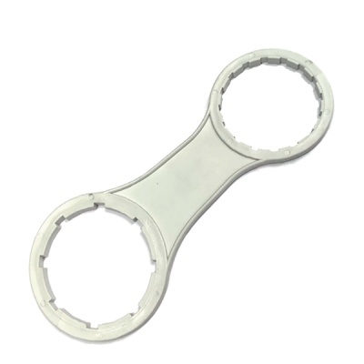 Chave dupla de plástico cinza claro com duas extremidades circulares dentadas.