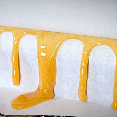 Líquido dourado viscoso escorrendo em gotas longas sobre fundo branco