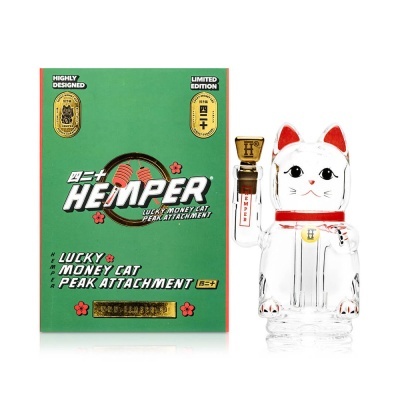 Cachimbo de vidro branco em forma de gato da sorte ao lado de caixa verde e dourada com texto.