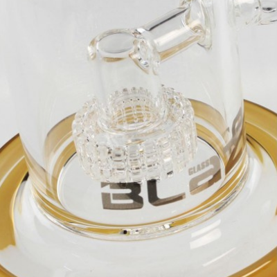 Detalhe de objeto em vidro transparente com texto 'BLO GLASS' e anel dourado na base