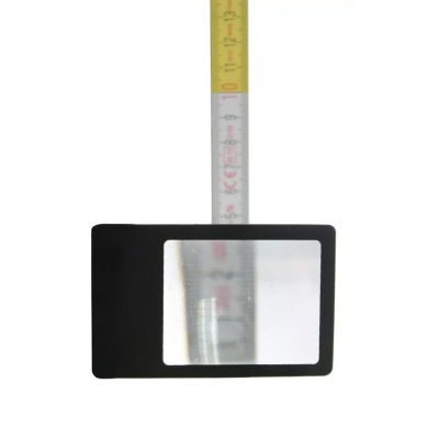 Lupa de mão preta com lente retangular diante de fita métrica amarela e branca