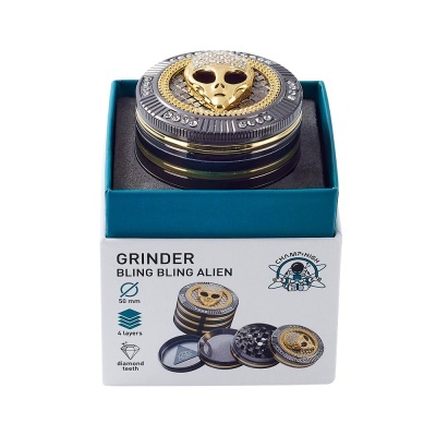 Triturador bling bling alien dourado com pedras numa caixa branca e azul