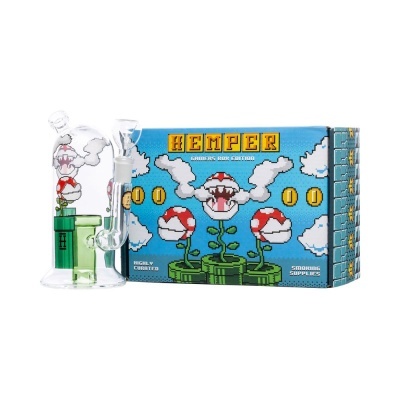 Equipamento de fumo em vidro com decoração pixelada e caixa azul com texto HEMPER GAMERS BOX EDITION