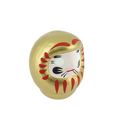 Figura Daruma dourada decorativa com rosto branco e detalhes vermelhos e pretos