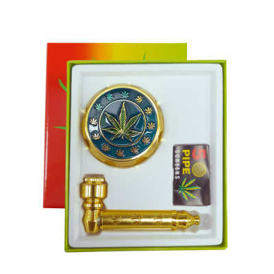 Conjunto para fumar com tubo dourado e triturador metálico com folhas de cannabis