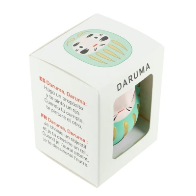 Caixa branca com figura Daruma verde água e dourada visível através de janela
