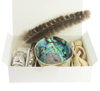 Conjunto de incenso e acessórios, incluindo sálvia, incenso e recipiente abalone numa caixa branca aberta.