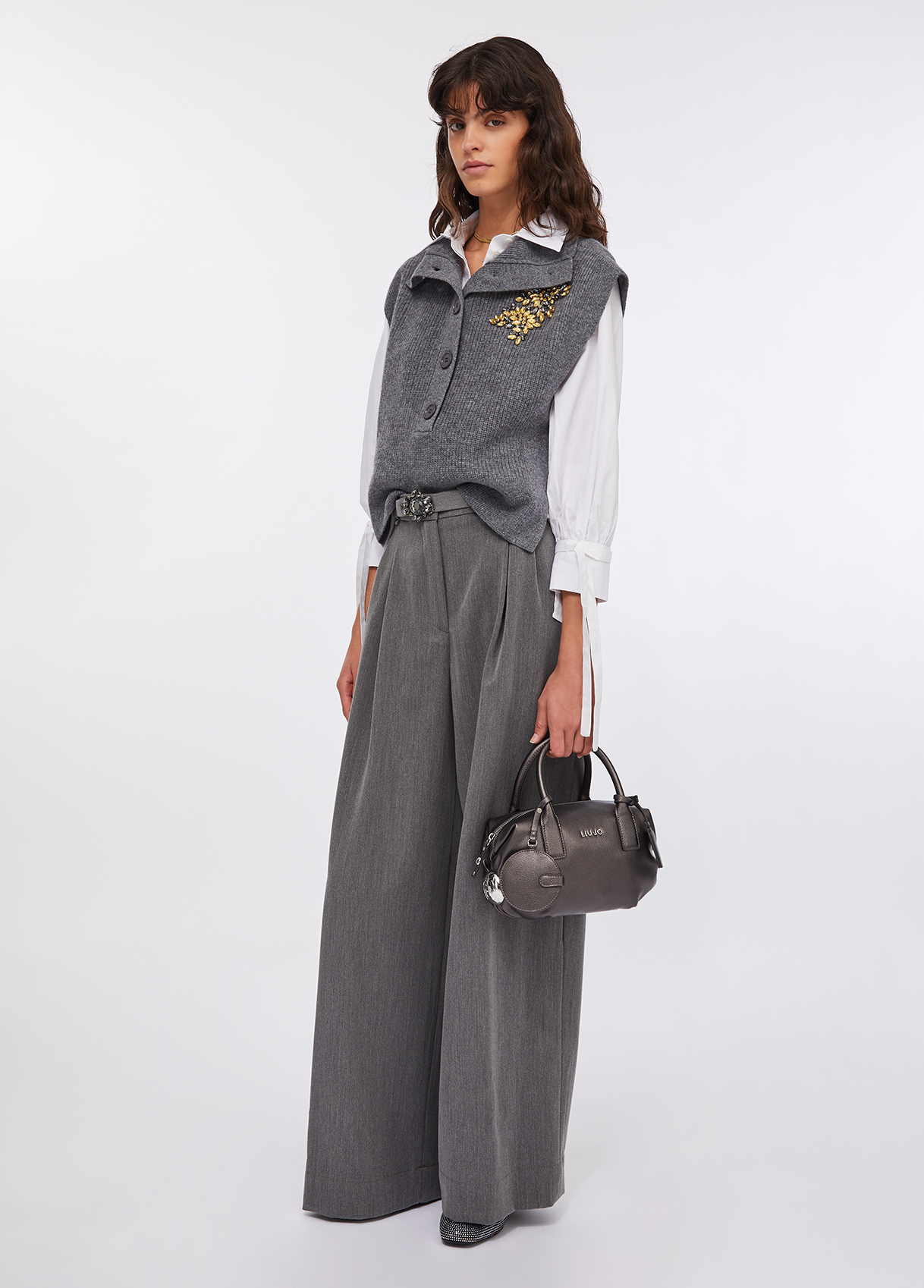 Palazzo trousers with belt Mulher de roupa cinzenta e branca com mala de mão prateada.