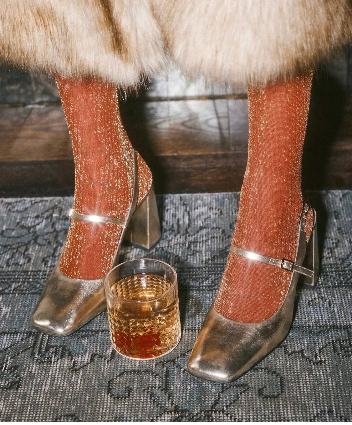 Sapatos dourados de salto quadrado com meias laranja brilhantes e copo de vidro com bebida