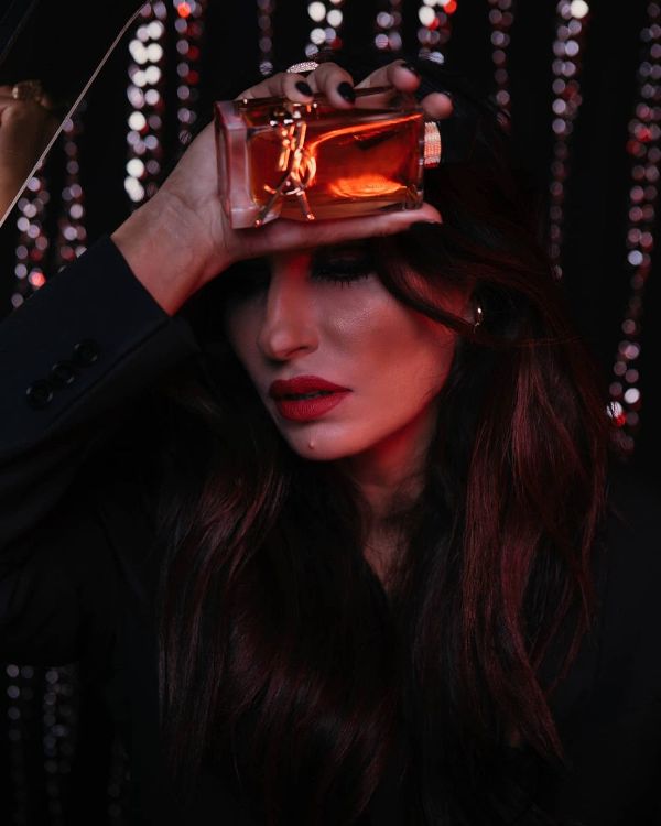 Frasco de perfume âmbar com detalhes dourados nas mãos de mulher com batom vermelho