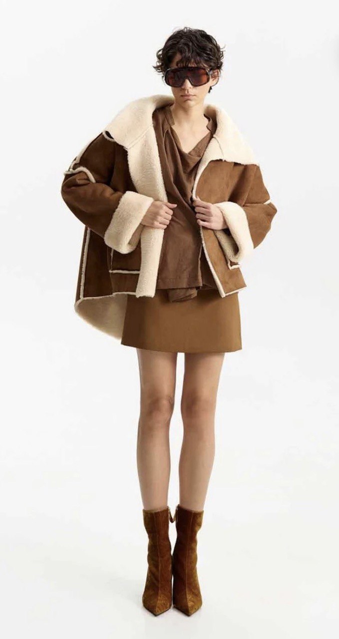 Camel Faux Shearling Jacket Pessoa com casaco castanho e creme, vestido castanho, botas castanhas e óculos escuros