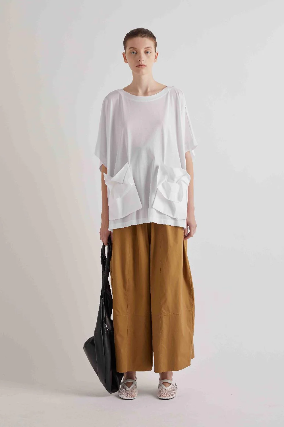 Balloon‑Line High‑Waisted Trousers with Buckles Modelo com t-shirt branca solta com bolsos, calças largas camel, sapatilhas brancas e mala preta