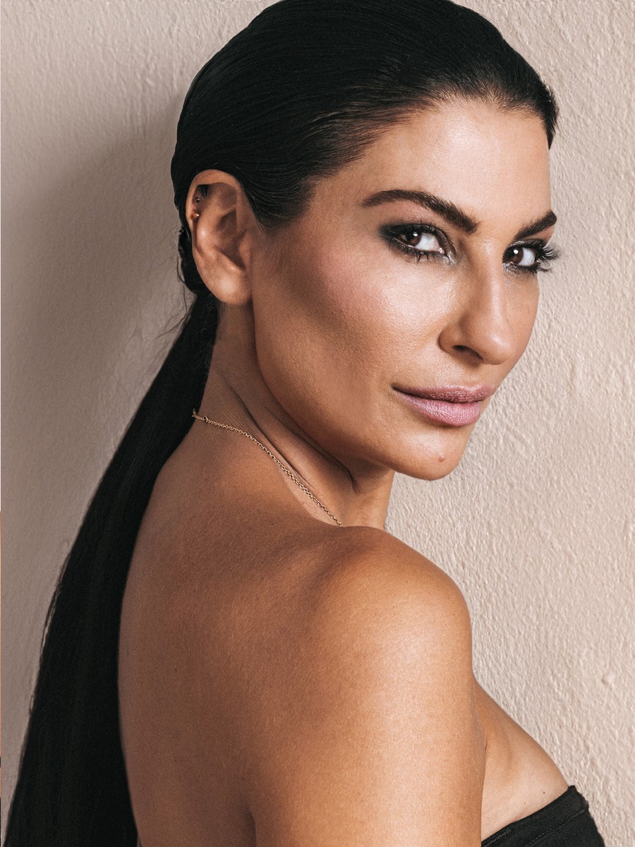 Mulher com cabelo preto liso e colar dourado posando de lado