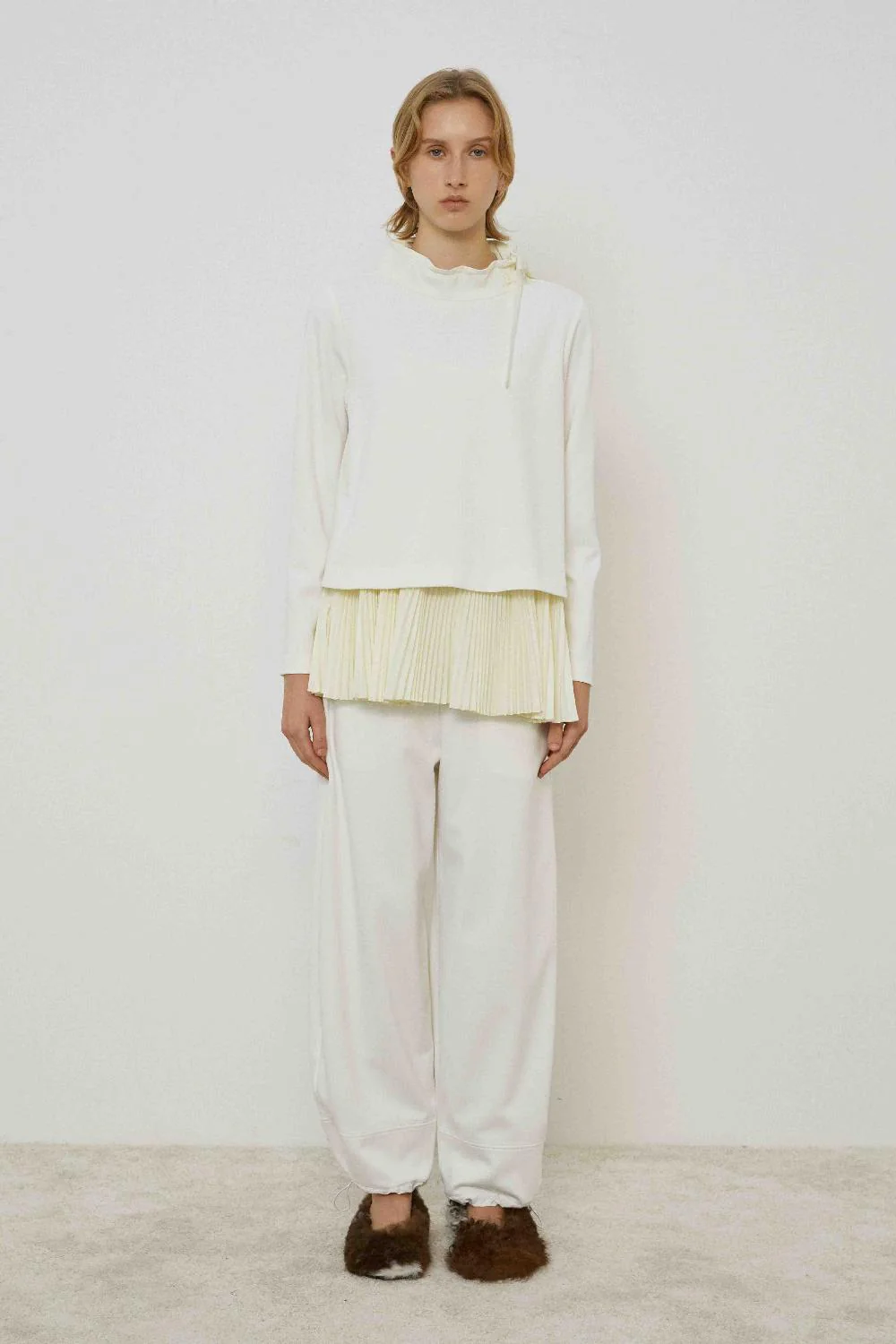 Straight-Leg Trousers with Taffeta Inserts Mulher com roupa branca e sapatilhas peludas castanhas em fundo branco simples.