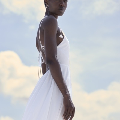 Mulher a usar vestido branco fluido com alças finas e amarração costas abertas.