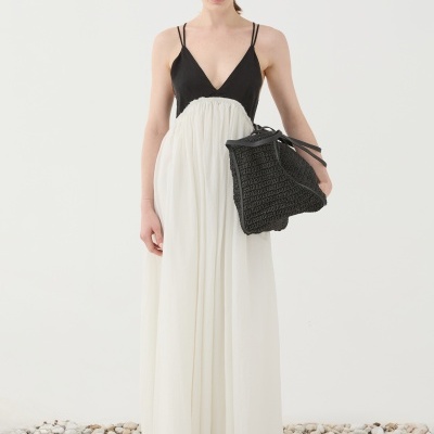 Vestido longo preto e branco com mala preta trançada em cenário com pedras.