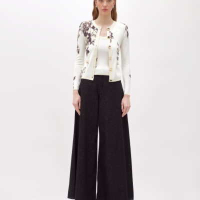 Mulher com camisola branca de padrão floral castanho e calças pretas largas em fundo branco