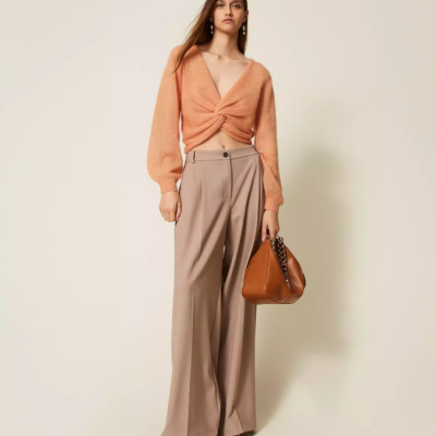 Mulher com camisola de malha pêssego e calças bege claro segura mala castanha