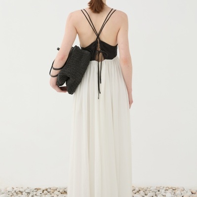 Vestido comprido preto e branco com alças finas e mala preta num fundo branco com pedras no chão.